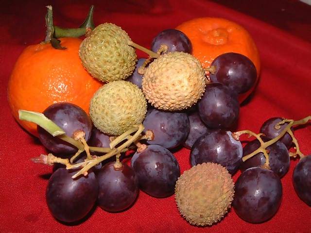 Food Fruit basket of lychees tangerines and black grapes on a bright red cloth