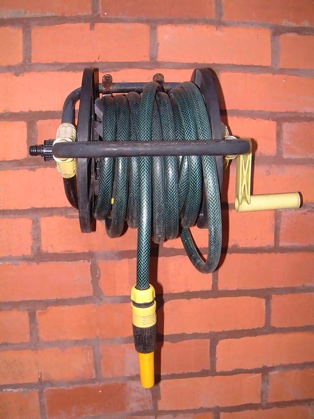 Miscellaneous Green host reel with yellow spout and winding handle attached to brick wall