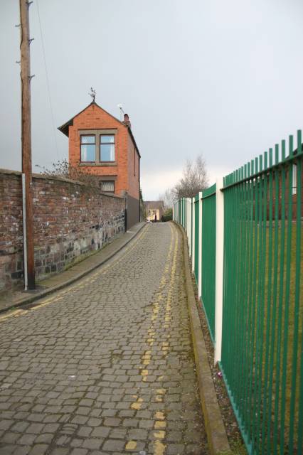 Narrow Cobbled Lane Running Between Metal Fence and House Wall